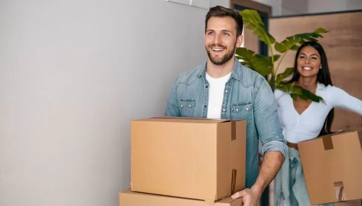 A smiling couple moving cardboard boxes into a new home.